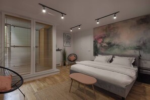 A modern bedroom with a large bed, a chair, a small table, and a painting on the wall. - Modern 2-Bed Apartment with 2 Bathrooms, Balcony (Kraków)