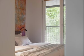 A bedroom with a bed, a window with blinds, and a wall with a textured artwork. - Modern 2-Bed Apartment with 2 Bathrooms, Balcony (Kraków)