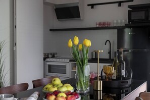 A modern kitchen with a stove, oven, and black refrigerator. There is a dining table with a bowl of apples and a vase of yellow tulips. - Modern 2-Bed Apartment with 2 Bathrooms, Balcony (Kraków)