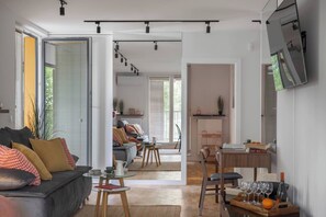 A modern living space with a sofa, dining table, and chairs, a kitchen area, and a TV mounted on the wall. - Modern 2-Bed Apartment with 2 Bathrooms, Balcony (Kraków)