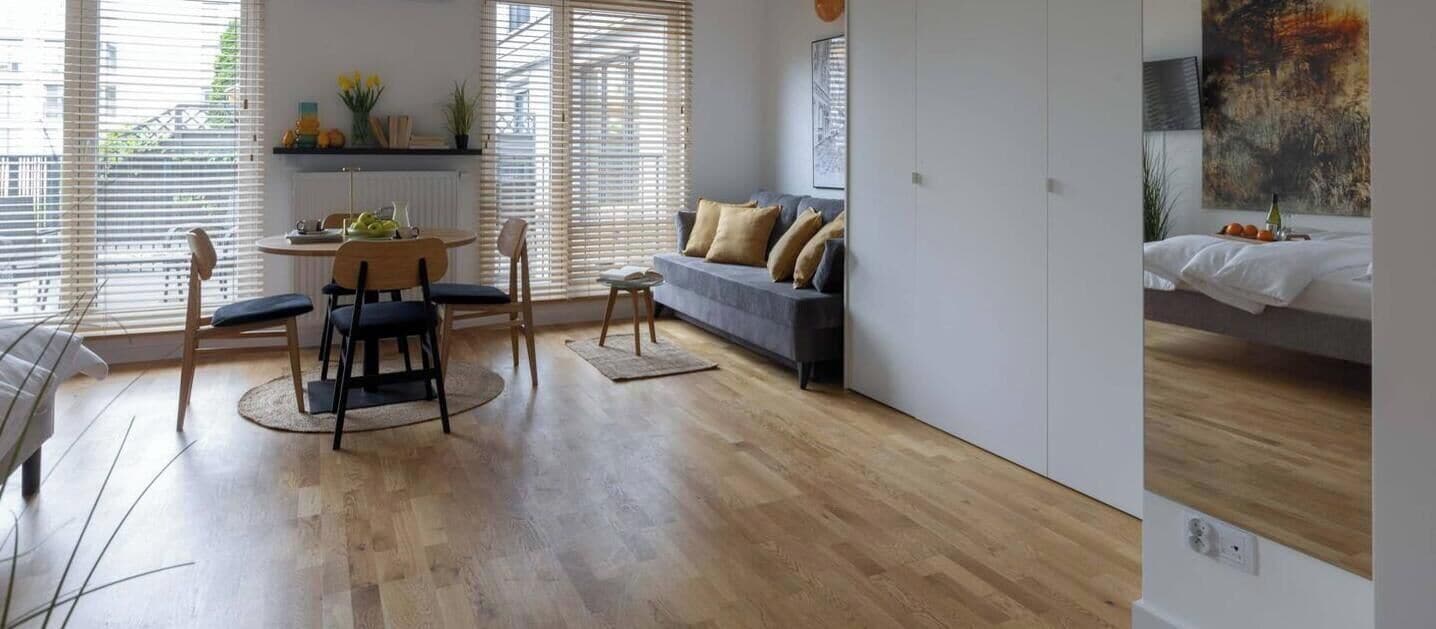 Ein modernes Wohnzimmer mit Essbereich, Holzboden und großen Fenstern mit Jalousien.