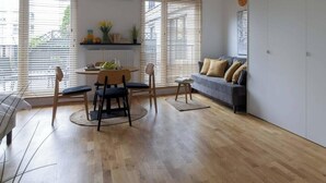 Un soggiorno moderno con zona pranzo, parquet e ampie finestre con tende.