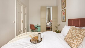 A bedroom with a bed, a desk, a chair, a mirror, and a wall with framed pictures. - Canvas House Porcelain 2-bed family apartment (Kraków)