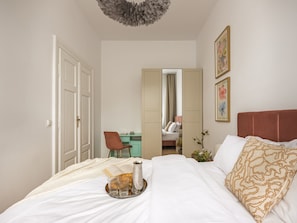 A bedroom with a bed, a desk, a chair, a mirror, and a wall with framed pictures. - Canvas House Porcelain 2-bed family apartment (Kraków)