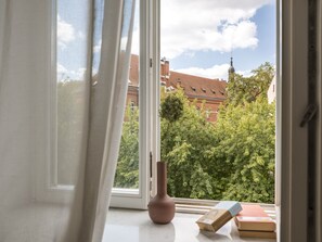 A window with a view of a brick building and trees. - Canvas House Porcelain 2-bed family apartment (Kraków)