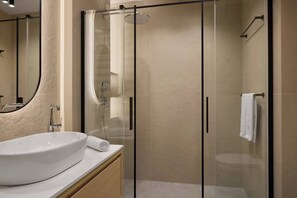 Un baño moderno con ducha de vidrio, un lavamanos blanco y un espejo.