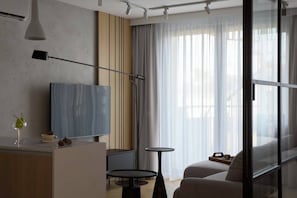 A modern hotel room with a large TV, a small table, a chair, and a sofa. - Vistula View Roof terrace 1-bed Apartment (Kraków)