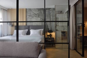 Una habitación de hotel moderna con una cama grande, una zona de estar separada, un separador de vidrio y vistas a la ciudad.