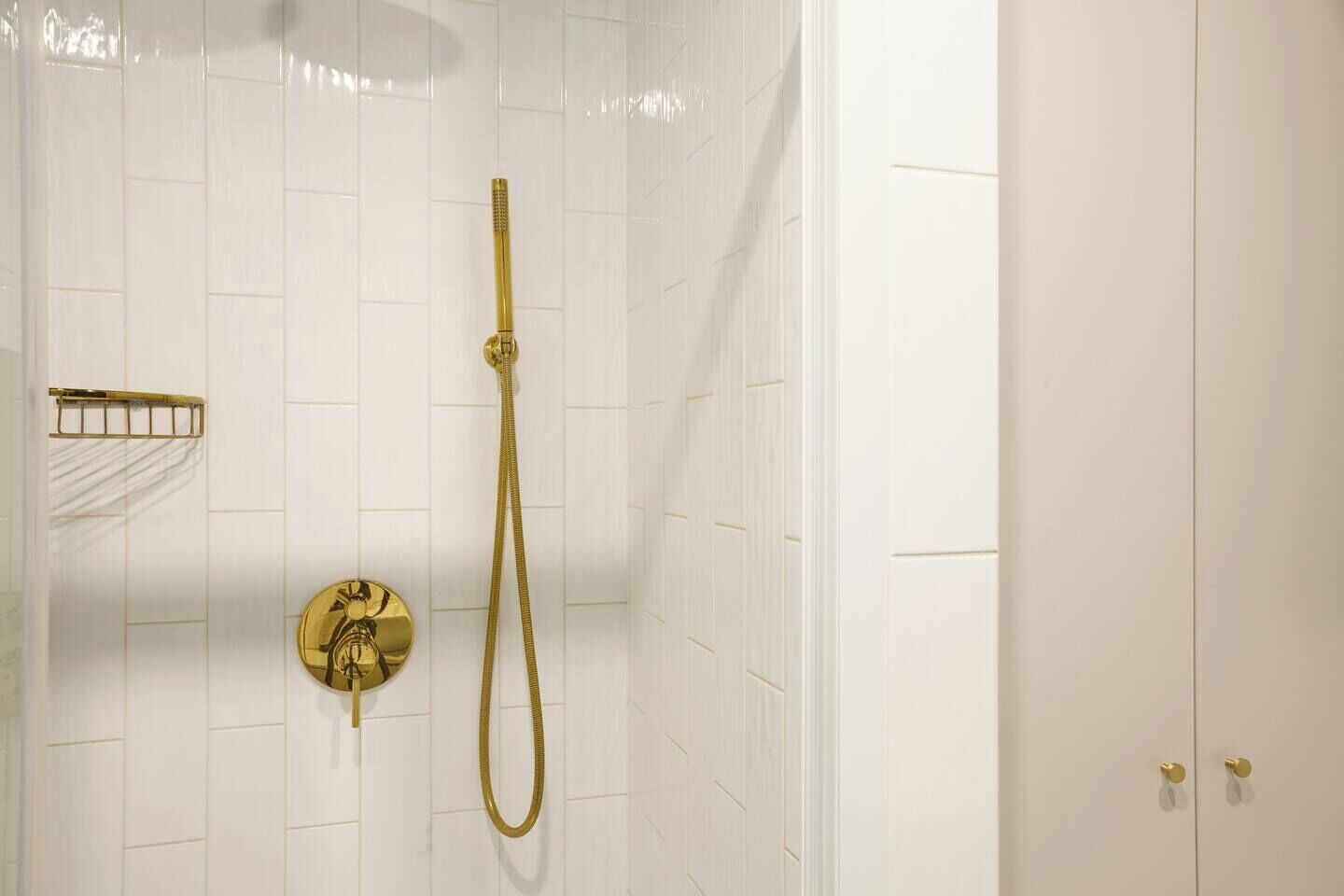 Een douche met een gouden douchekop en slang, een handdoekhouder en een bedieningspaneel aan de muur.