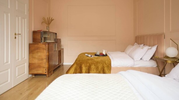 Een hotelkamer met twee bedden, een houten dressoir, een nachtkastje met een lamp en een deur.