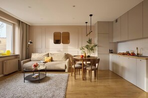 Ein modernes Wohnzimmer mit Sofa, Couchtisch und Esstisch mit Stühlen. Es gibt eine Küchenzeile mit Schränken und einer Arbeitsplatte.