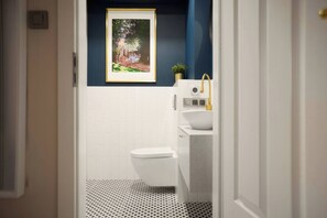 A bathroom with a white toilet, a sink with a gold faucet, and a framed picture on the wall. - Polka Apartment 2-bed (Kraków)