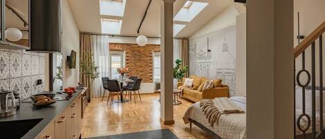 A modern interior with a kitchen, dining area, and bedroom, featuring skylights, wooden flooring, and a loft-style bed.