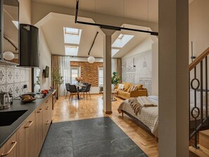 Ein modernes Interieur mit Küche, Essbereich und Schlafzimmer, ausgestattet mit Dachfenstern, Holzböden und einem Schlafbett im Loft-Stil.
