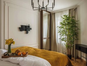 A bedroom with a bed, a bedside table, a potted plant, and a window with curtains. - 2-bedroom classy apartment near Planty Park (Kraków)