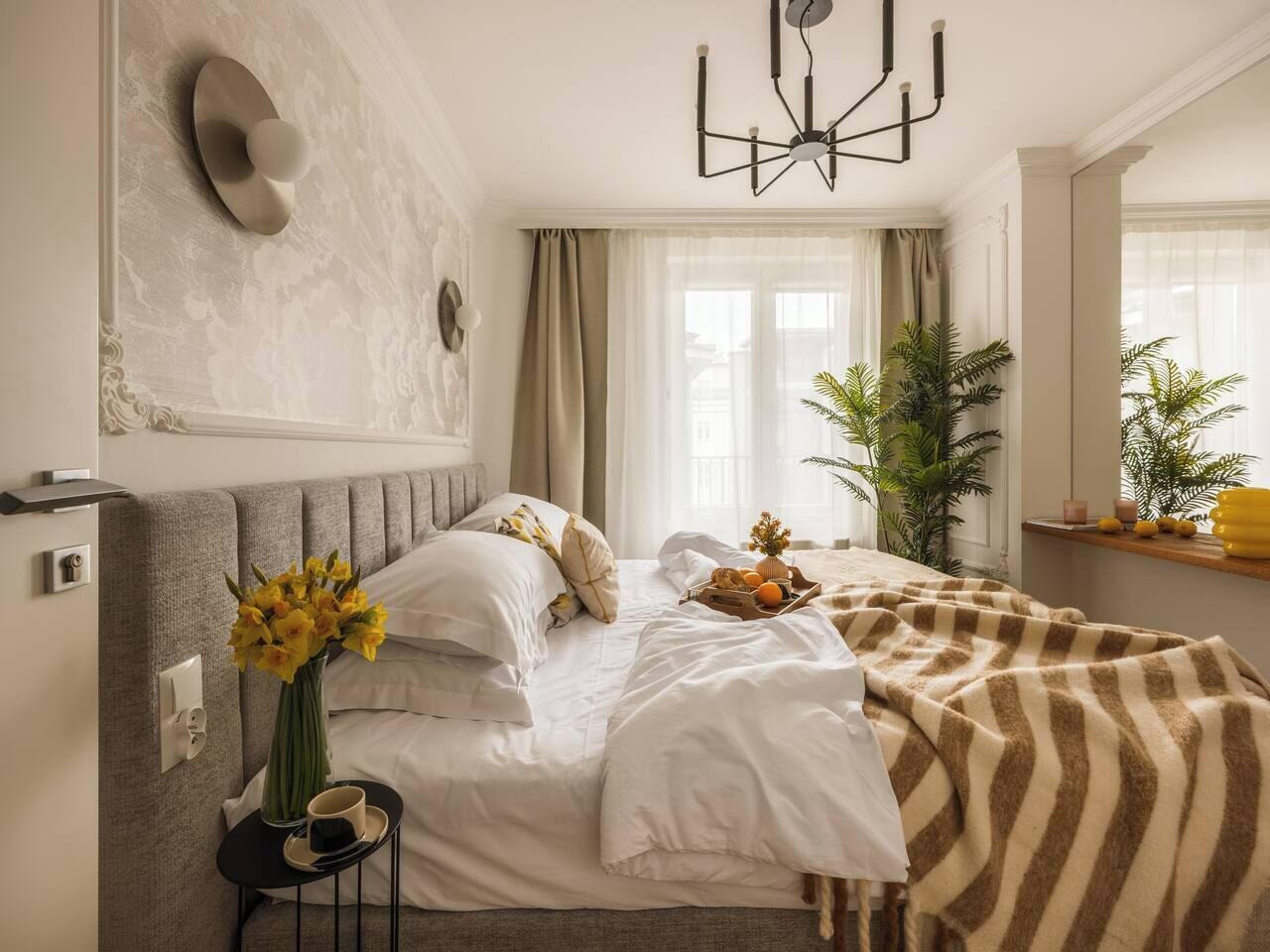 Un letto rifatto con una coperta a righe, un comodino con un vaso di fiori e un lampadario moderno.