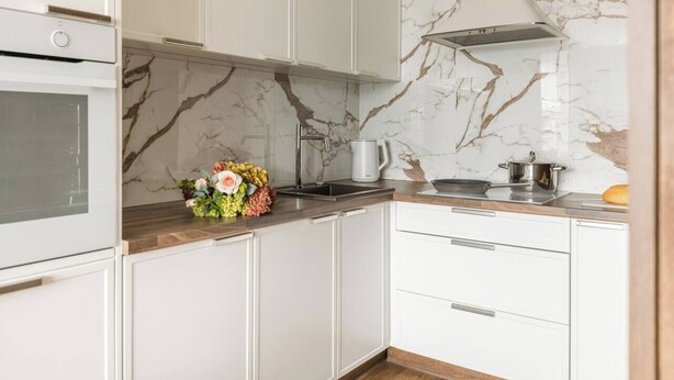 Eine moderne Küche mit weißen Schränken, einer Marmor-Spritzschutzwand und einem eingebauten Backofen.