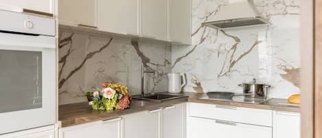A modern kitchen with white cabinetry, a marble backsplash, and a built-in oven.