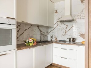 A modern kitchen with white cabinetry, a marble backsplash, and a built-in oven. - Vistula View 1-bed Apartment (Kraków)