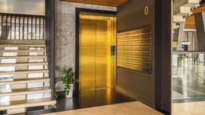 Ein moderner Aufzug mit Metalloptik, ein an der Wand montierter Briefkasten und eine Treppe mit Holzhandlauf.