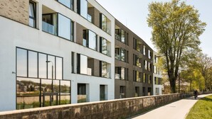 Ein modernes Gebäude mit mehreren Etagen, großen Fenstern und einem gepflasterten Weg.