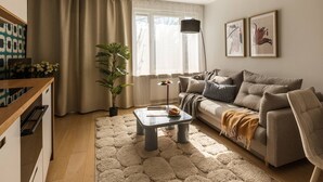 Una sala de estar con sofá, una mesita de centro, una planta y un ventanal con cortinas.
