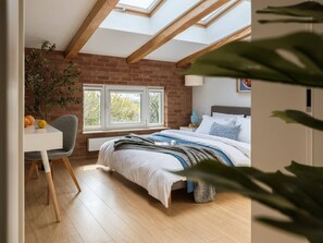 A bedroom with a brick wall, a skylight, a bed, a bedside table, a chair, and a window. - 2-bed Apartment by the Planty Park (Kraków)