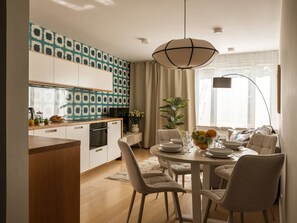 A modern kitchen with a dining area, wooden cabinets, a large window, and a hanging light fixture. - 2-bed Apartment by the Planty Park (Kraków)