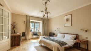 Ein Schlafzimmer mit Bett, Nachttischen, Schreibtisch, Stuhl, einem Fenster mit Vorhängen und einer Kristallleuchter.