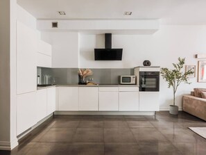 A modern kitchen with white cabinetry, a black range hood, a microwave, and an oven. - Bauhaus Apartment 1-bed (Kraków)