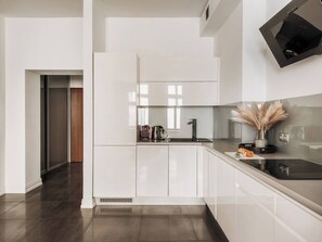 A modern kitchen with white cabinetry, a black countertop, and a built-in oven. - Bauhaus Apartment 1-bed (Kraków)