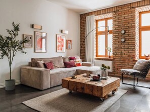 A living room with a sofa, a coffee table, a potted plant, and a brick wall. - Bauhaus Apartment 1-bed (Kraków)