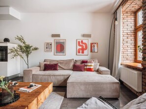 A modern living room with a sofa, ottoman, coffee table, and wall art. - Bauhaus Apartment 1-bed (Kraków)