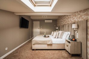 A bedroom with a skylight, a bed, a nightstand, a TV, and a door. - White Lotus - penthouse with roof terrace (Kraków)