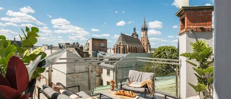 Eine Dachterrasse mit Sitzgelegenheiten im Freien, Blick auf ein historisches Gebäude und einen klaren Himmel.