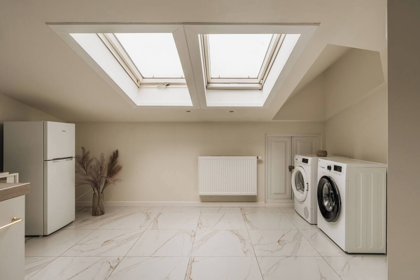 A modern kitchen with a skylight, a refrigerator, a washing machine, and a radiator.