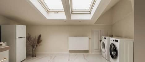 A modern kitchen with a skylight, a refrigerator, a washing machine, and a radiator.