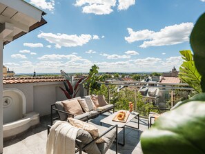 Una terraza con sofá, mesa y sillas, con vistas a un paisaje urbano con edificios y cielo despejado.