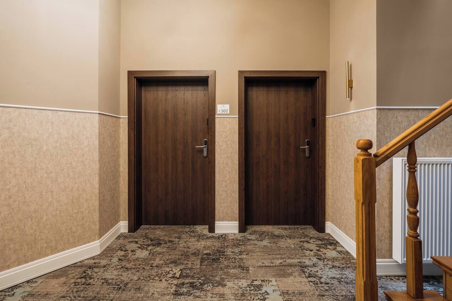 Ein Korridor mit zwei Holztüren, einem Teppichboden und einer Holztreppe.
