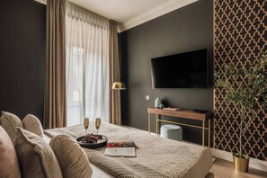 A modern living room with a large flat-screen TV, a dining table with two chairs, a sofa, a potted plant, and a decorative wall panel. - White Lotus - 2-bed apartment, full kitchen (Kraków)