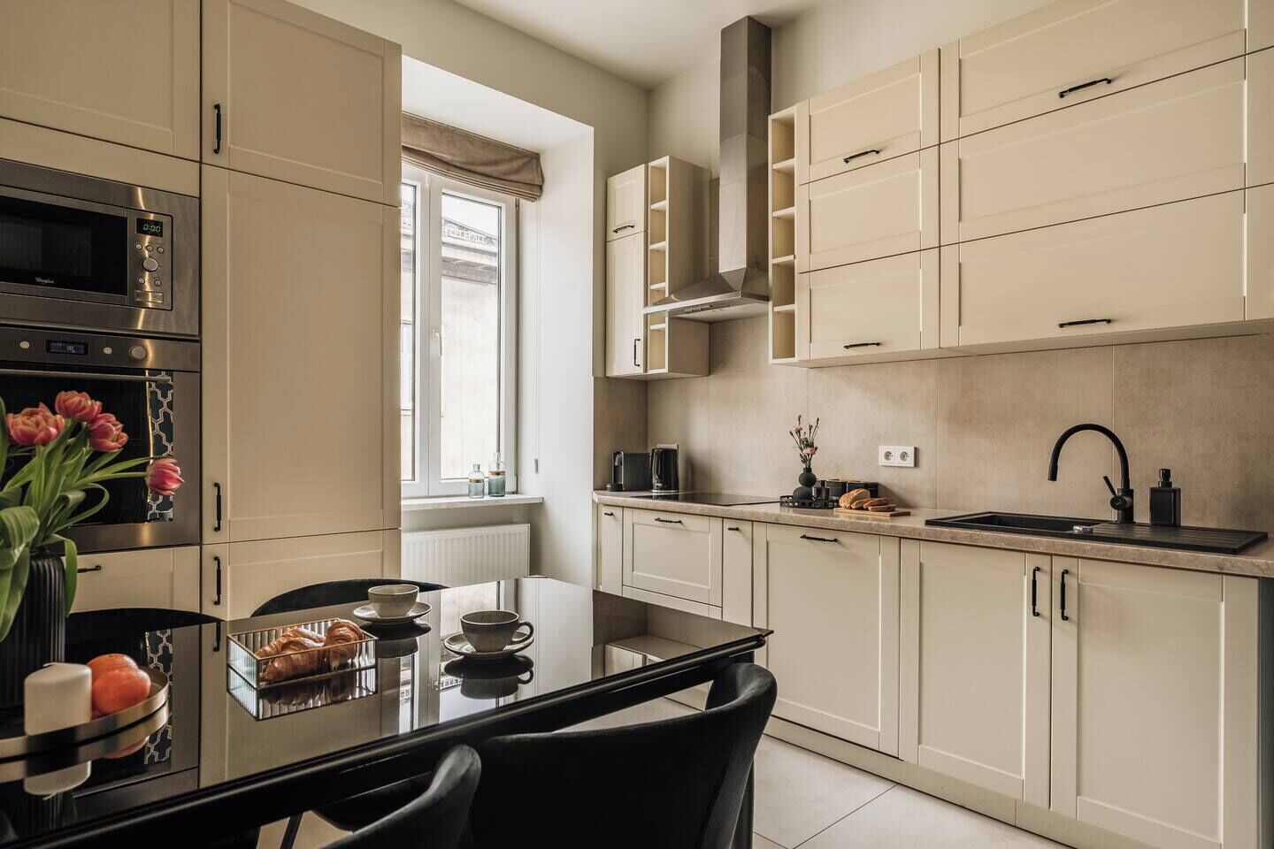 A modern kitchen with a dining area, featuring a built-in oven, a microwave, a sink, and a window with a view.