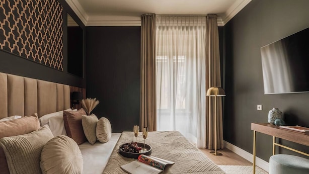 Ein modernes Hotelzimmer mit einem großen Bett, einem Nachttisch, einem Fernseher und einem Fenster mit Vorhängen.