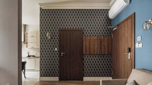 Ein Zimmer mit strukturiertem Wandpapier, einem Holzschrank, einem beigefarbenen Sofa und einer Küchenzeile mit Schränken und einer Arbeitsplatte.