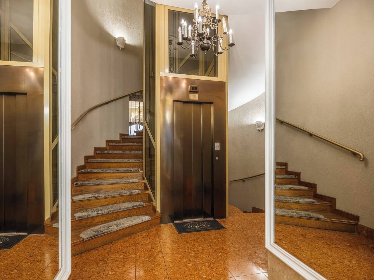 Een glanzende houten trap met een spiegelwand, een lift en een kroonluchter.