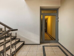 A staircase with metal railings, a door leading to a hallway, and a tiled floor. - Green Boho 2-bed family apt in the city center (Kraków)