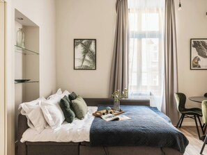 A neatly made bed with pillows, a tray with items, and a framed picture on the wall. - Green Boho 2-bed family apt in the city center (Kraków)