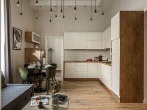 A modern kitchen with white cabinets, a wooden accent wall, and pendant lighting. - Green Boho 2-bed family apt in the city center (Kraków)