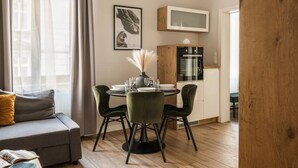 A modern living room with a gray sofa, a dining table with four chairs, and a kitchen area with a microwave and cabinets. - Green Boho 2-bed family apt in the city center (Kraków)
