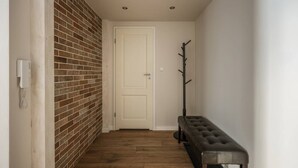 A hallway with a brick wall, a white door, a bench, and a coat rack. - Green Boho 2-bed family apt in the city center (Kraków)
