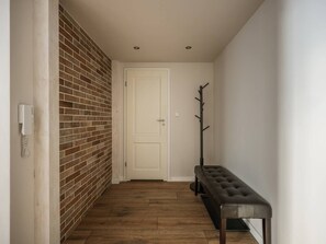 A hallway with a brick wall, a white door, a bench, and a coat rack. - Green Boho 2-bed family apt in the city center (Kraków)